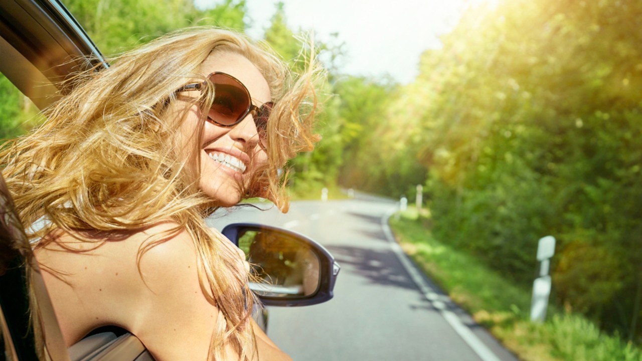 Lachende Frau schaut aus fahrendem Auto