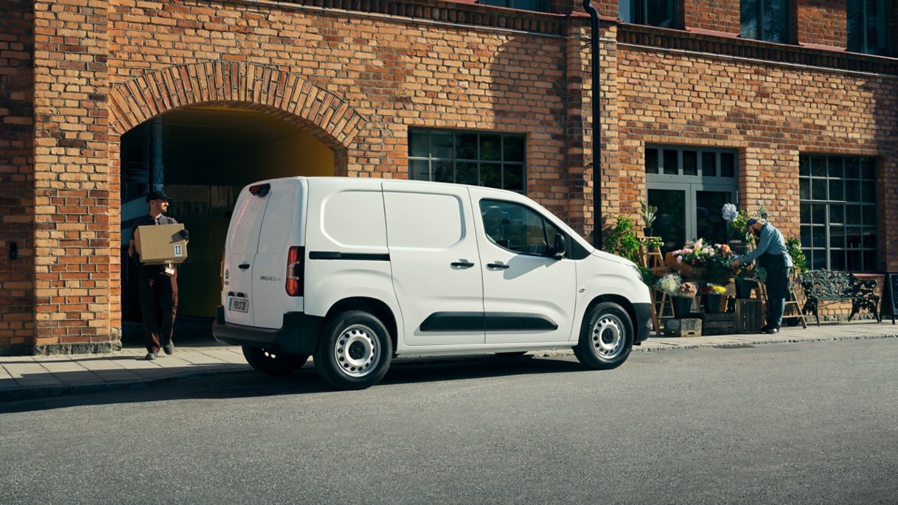 Ein weißer Proace City Electric steht vor einem Ladengeschäft, aus dem ein Paketbote herauskommt.