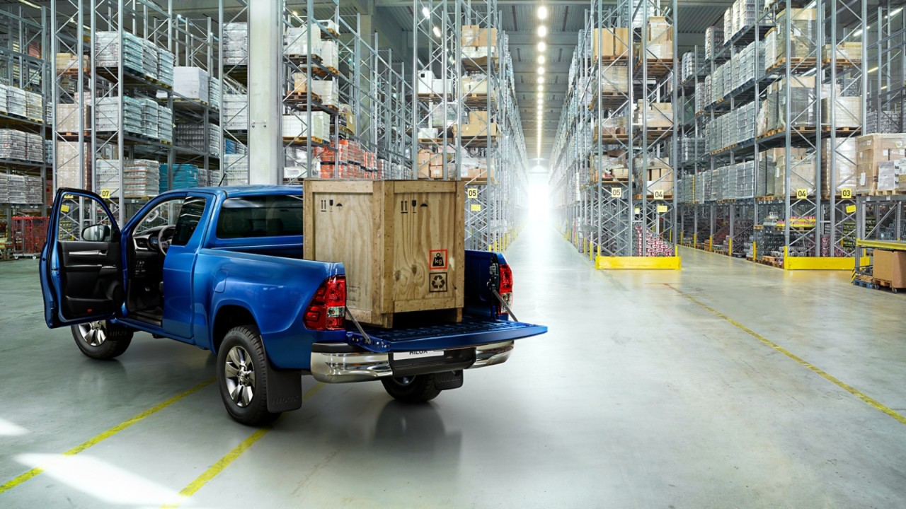 Ein blauer Toyota Hilux steht geparkt in einer Lagerhalle mit einer Holzkiste auf der Ladefläche.
